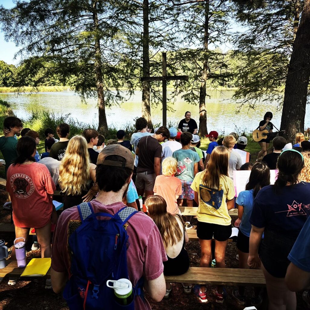 Campers sing songs at the outdoor chapel by the lake at Camp Bratton-Green